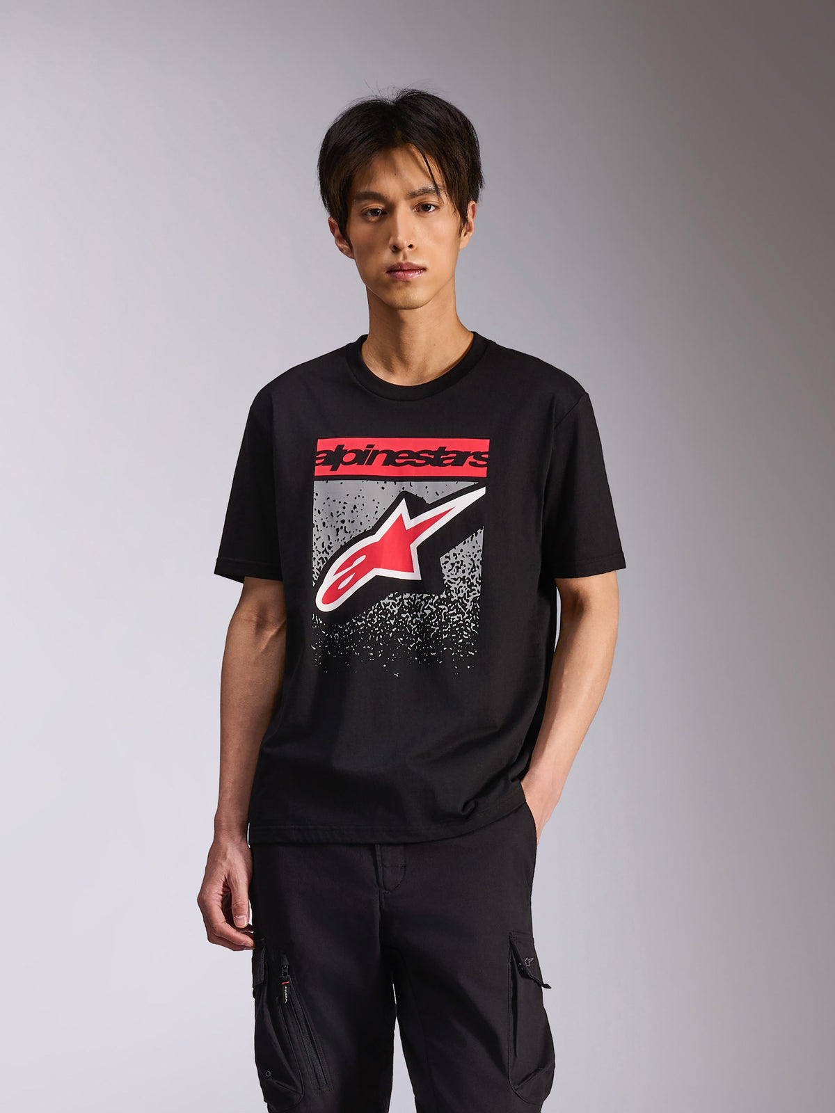 Alpinestars Noka CSF Tee, t-shirt de manga curta, preta, com texto Alpinestars a vermelho e logótipo Astars a vermelho e branco com uma gradação MX cinzenta salpicada, streetwear casual inspirado no desporto motorizado