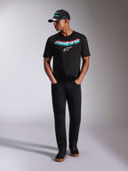 T-shirt Alpinestars Ellipsoid CSF, t-shirt de manga curta, preta, com a palavra Astars curvada em gradiente azul-turquesa e cor-de-rosa e logótipo branco, usada por um modelo com boné e calças pretas a condizer, vestuário casual de estilo de vida motorsport