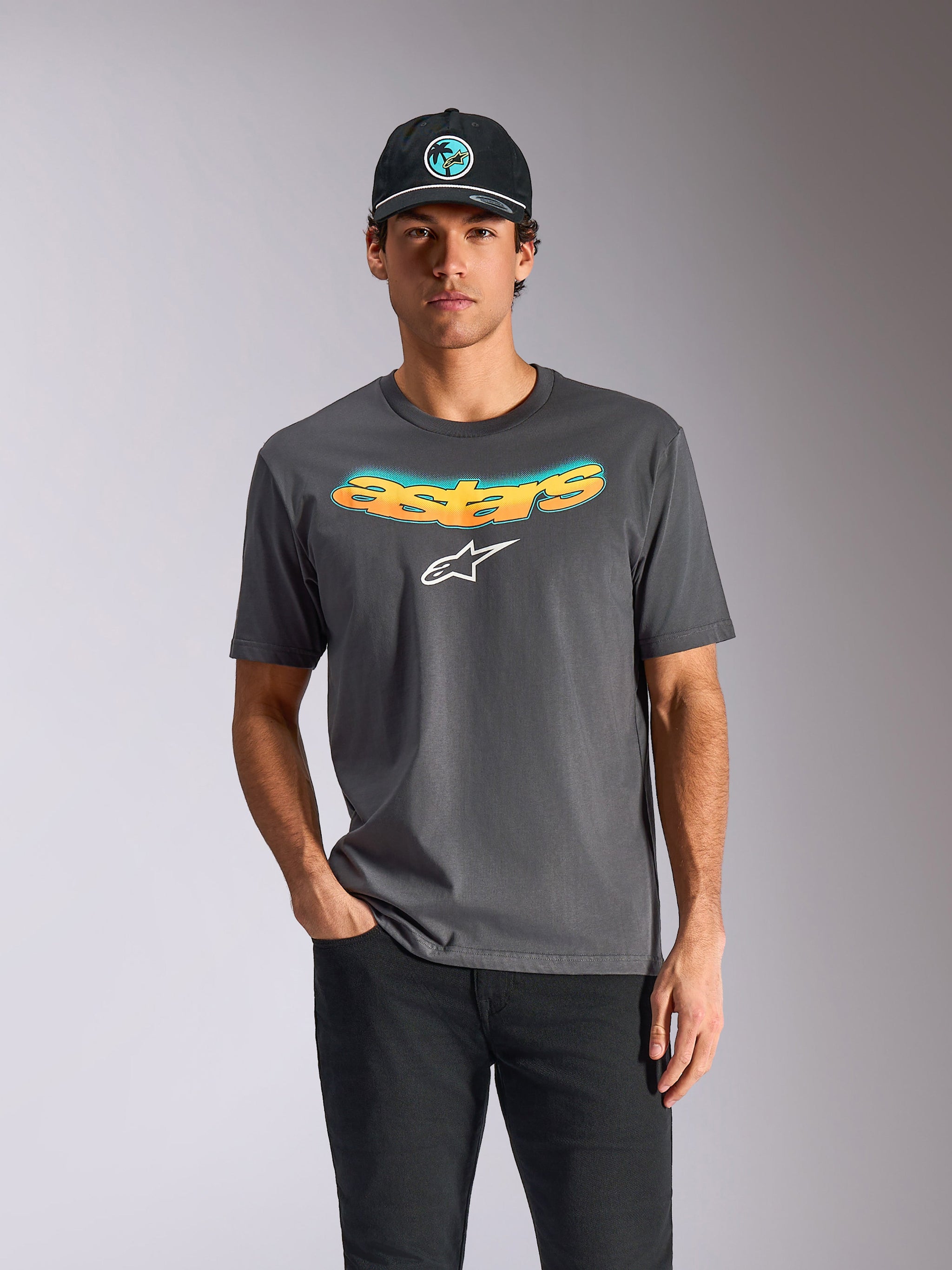 Alpinestars Ellipsoid CSF Tee, Short Sleeve T-Shirt, Charcoal Gray, curved "astars" wordmark with orange and blue gradient and a white logo, worn by a model with a black cap and pants, casual motorsport streetwear