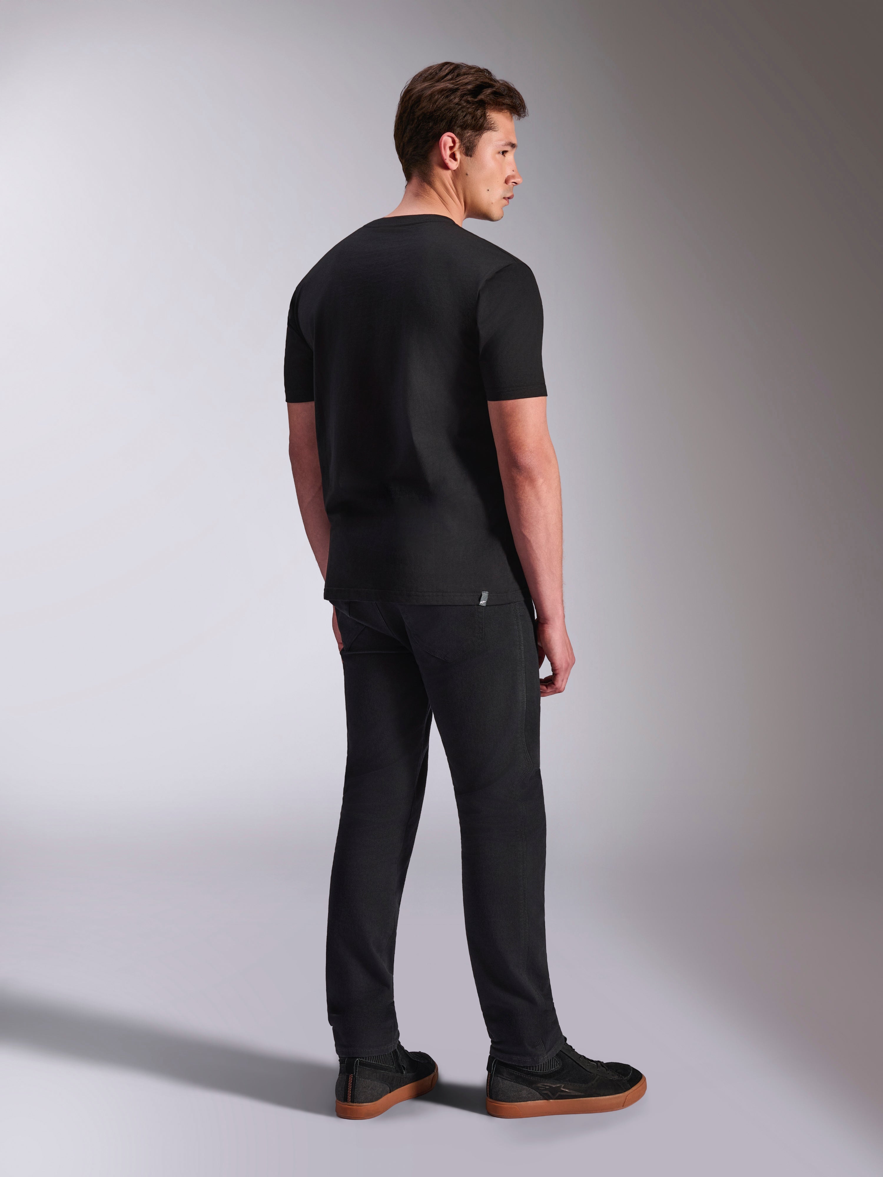 Alpinestars Abus CSF Tee, t-shirt de manga curta, preta, vista traseira num modelo masculino, streetwear casual de motorsport, combinada com calças escuras e sapatilhas