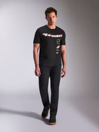 T-shirt Alpinestars Abus CSF, T-shirt de manga curta, preta, logótipo curvo a vermelho e branco com vários logótipos sobrepostos, usada por um modelo masculino com calças pretas e sapatilhas pretas, streetwear casual de desportos motorizados
