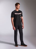Alpinestars Abus CSF Tee, T-shirt de manga curta, preta, com logótipo Alpinestars curvo em vermelho e branco e gráficos empilhados verticalmente, usada com calças pretas e sapatilhas, streetwear casual inspirado no desporto motorizado