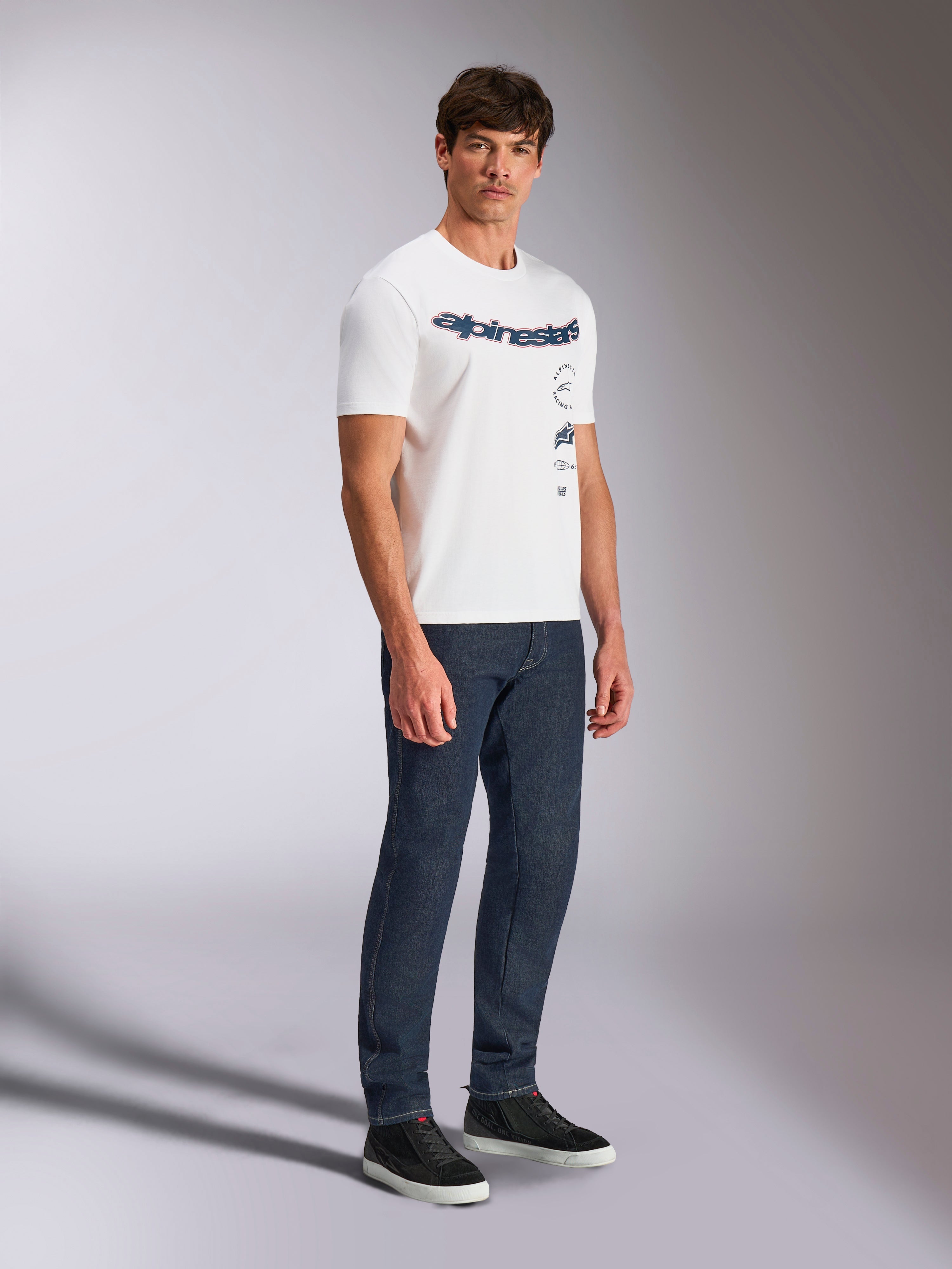 Alpinestars Abus CSF Tee, Short Sleeve T-Shirt, White, Multi-stacked Alpinestars curved logo design, worn by male model with dark blue jeans and black sneakers, casual motorsport streetwear