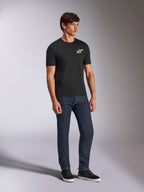 Alpinestars Angler CSF Tee, t-shirt de manga curta preta com logótipo Astars vibrante e multicolor no peito, modelo masculino com calças de ganga azul escura e sapatilhas pretas, vestuário casual de estilo streetwear e motorsport