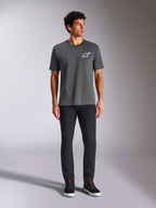 Alpinestars Angler CSF Tee, t-shirt de manga curta, cor Charcoal, com um logótipo Astars vibrante e multicolor no peito, vestida por um modelo com calças pretas e sapatilhas, Casual Motorsport Streetwear