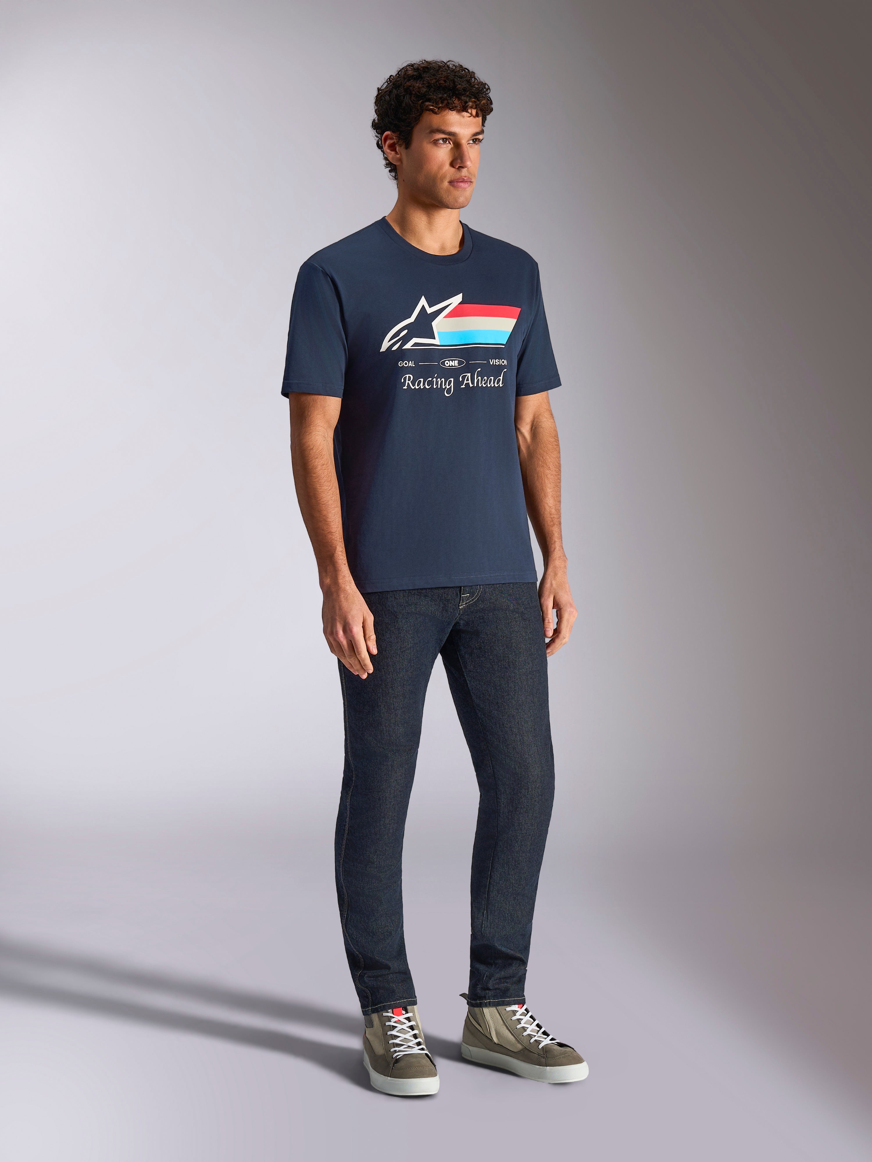Alpinestars Trifecta CSF Tee, Short Sleeve T-Shirt, Navy Blue, featuring Astars logo with tri-color stripes and Racing Ahead text, worn by a model with dark jeans and sneakers, casual motorsport-inspired streetwear