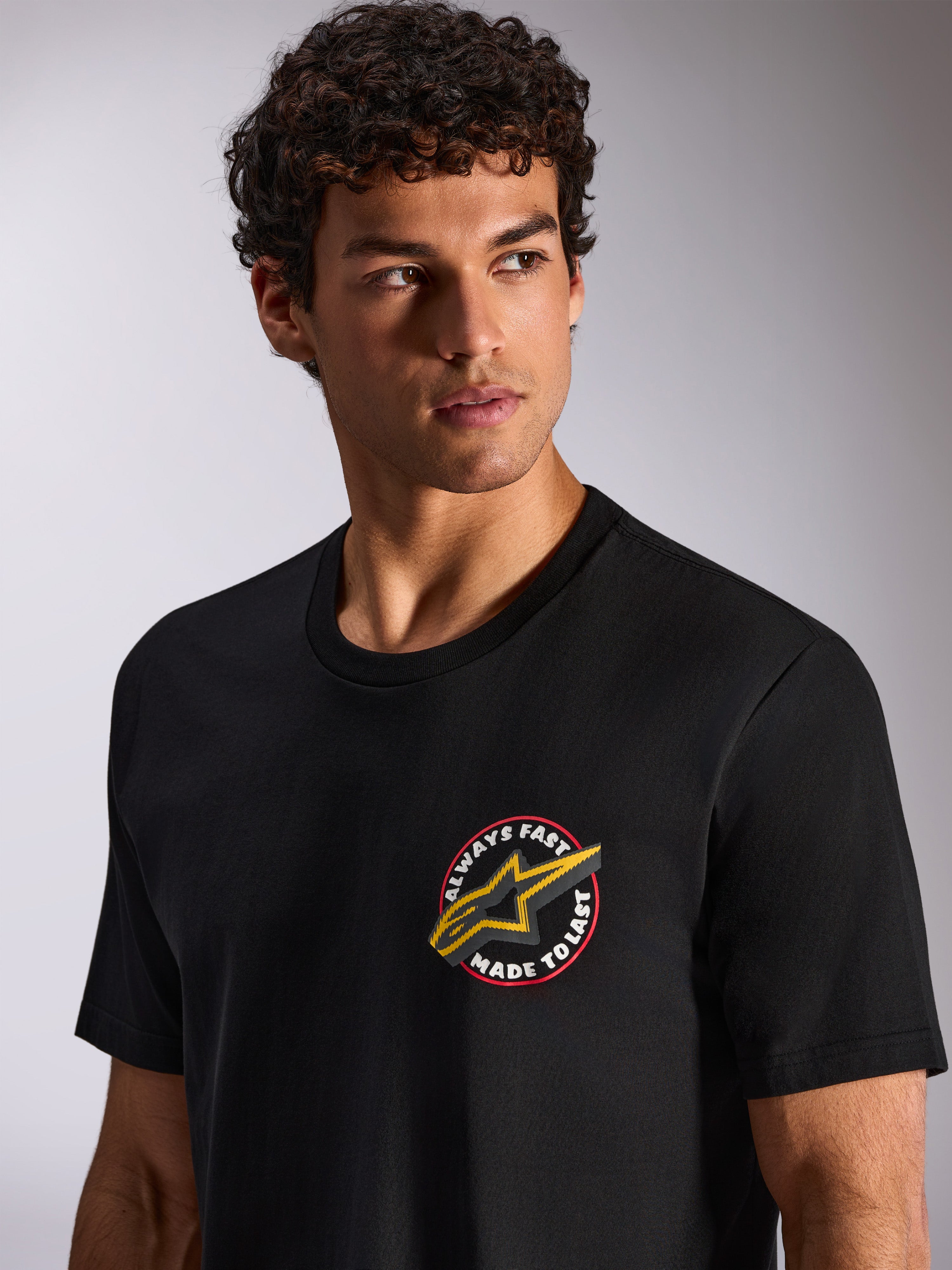 T-shirt Alpinestars Aorbit CSF, t-shirt de manga curta, preta, gráfico circular no peito "Always Fast Made to Last" com logótipo Astars amarelo, vestida por modelo, streetwear casual de desportos motorizados