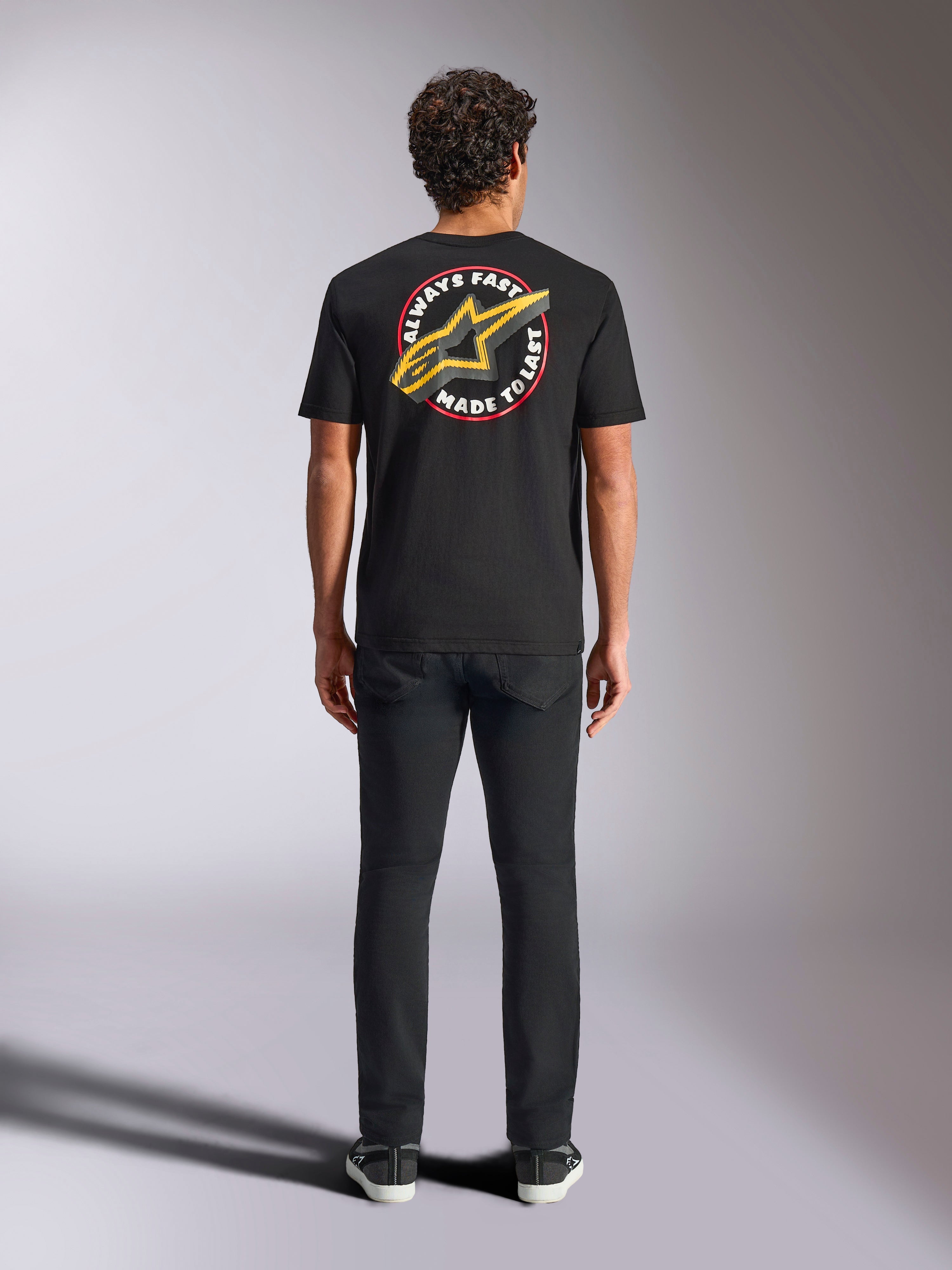 Alpinestars Aorbit CSF Tee, t-shirt de manga curta, preta, vista de costas num modelo com calças pretas, com um gráfico grande 'Always Fast Made to Last' e logótipo Astars amarelo, streetwear casual de desportos motorizados