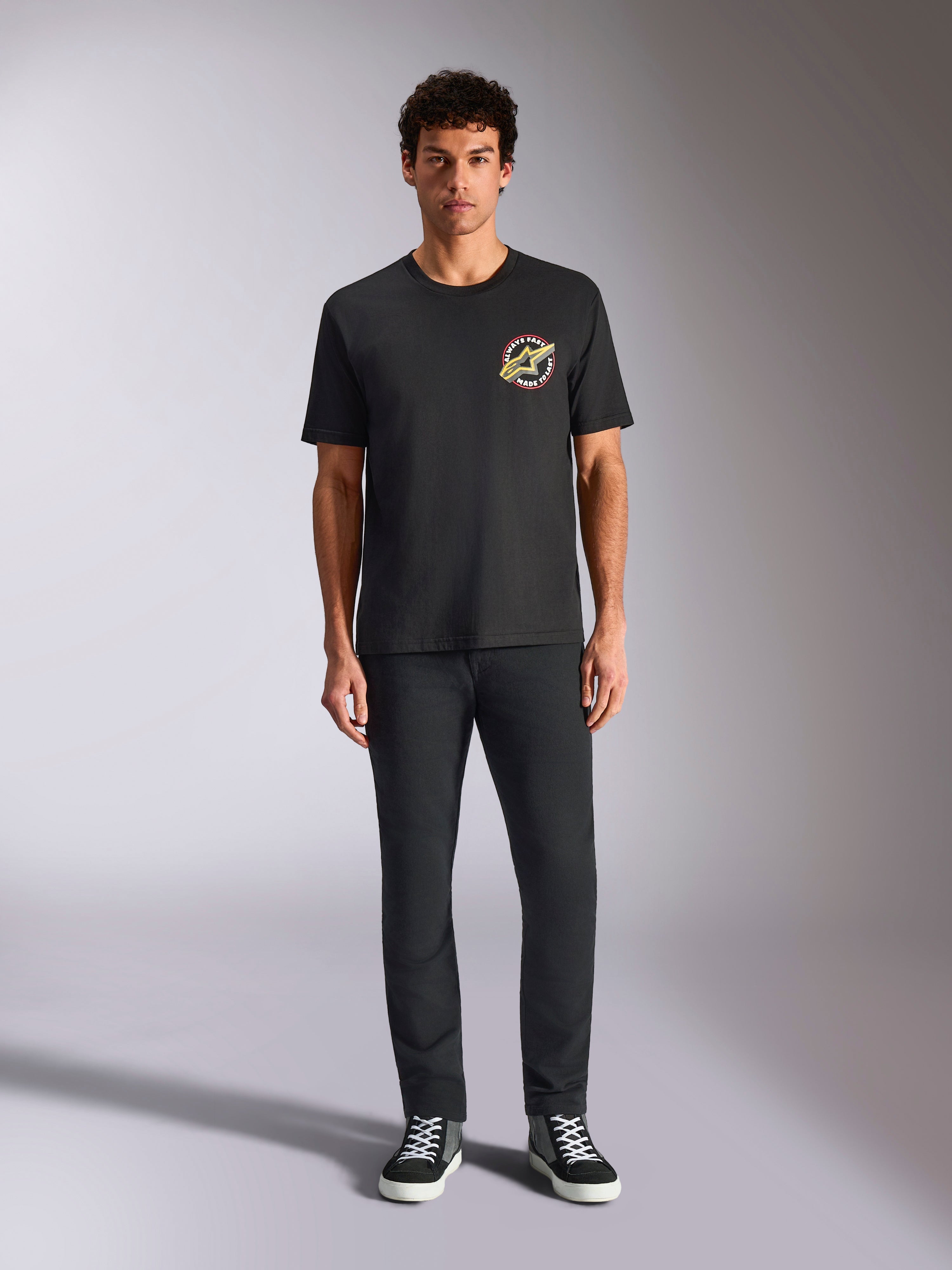 Alpinestars Aorbit CSF Tee, t-shirt de manga curta, preta, logótipo circular com o texto 'Always Fast Made to Last' no peito, usada por um modelo com calças pretas e sapatilhas, streetwear casual inspirado no desporto motorizado