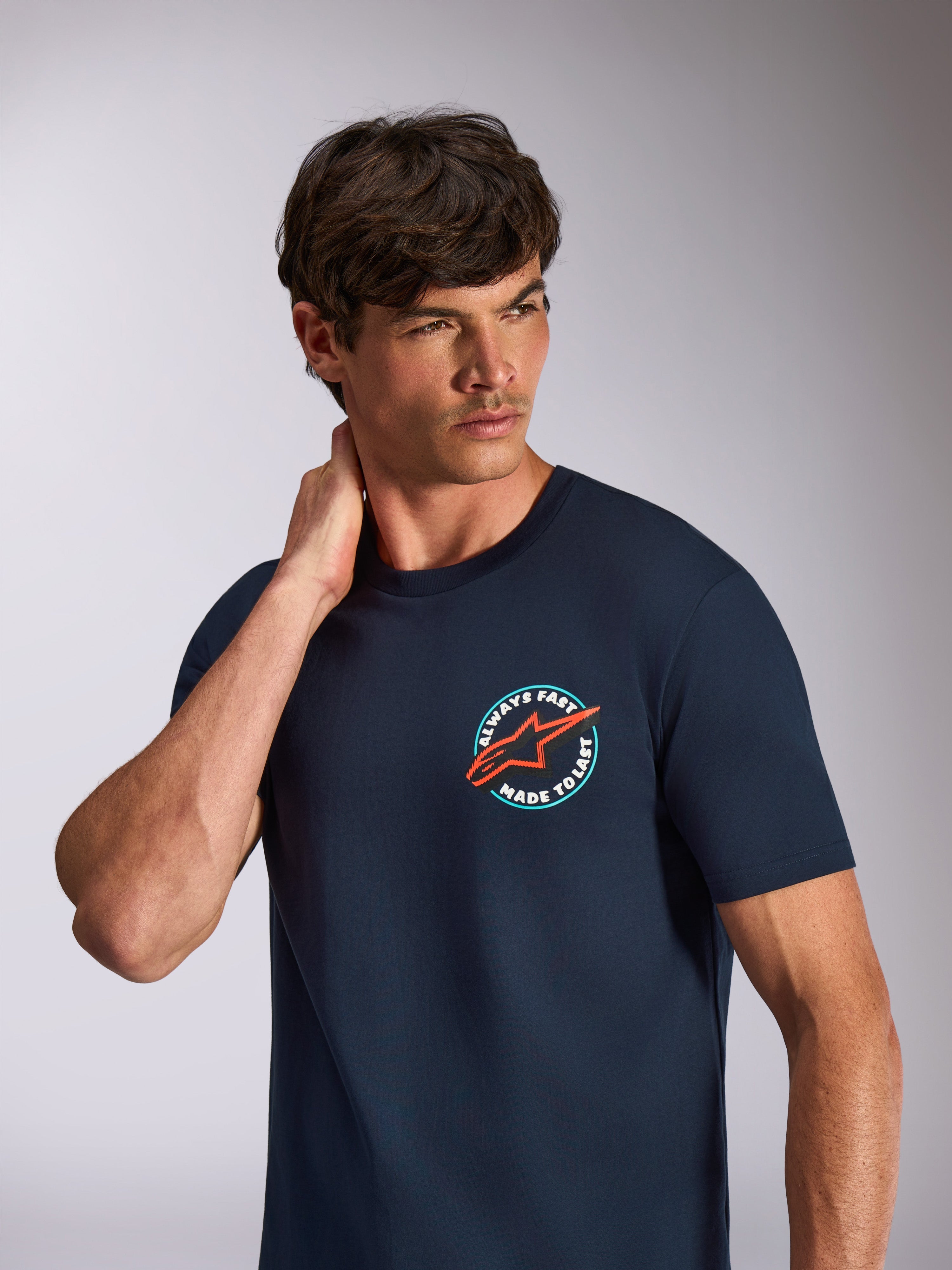 Alpinestars Aorbit CSF Tee, t-shirt de manga curta, azul marinho, gráfico circular no peito com logótipo de estrela cor-de-laranja e texto "Always Fast Made to Last", streetwear casual de desportos motorizados