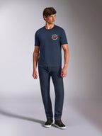 T-shirt Alpinestars Aorbit CSF, t-shirt de manga curta, azul marinho, gráfico circular no peito com o texto "Always Fast Made to Last", usada com calças de ganga escuras e sapatilhas, vestuário casual de estilo de vida motorsport
