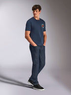 Alpinestars Aorbit CSF Tee, t-shirt de manga curta, azul-marinho, com logótipo Astars circular em cor de laranja e branco e o gráfico Always Fast Made to Last, usada por um homem com calças de ganga escuras e sapatilhas pretas, streetwear casual inspirado no desporto motorizado