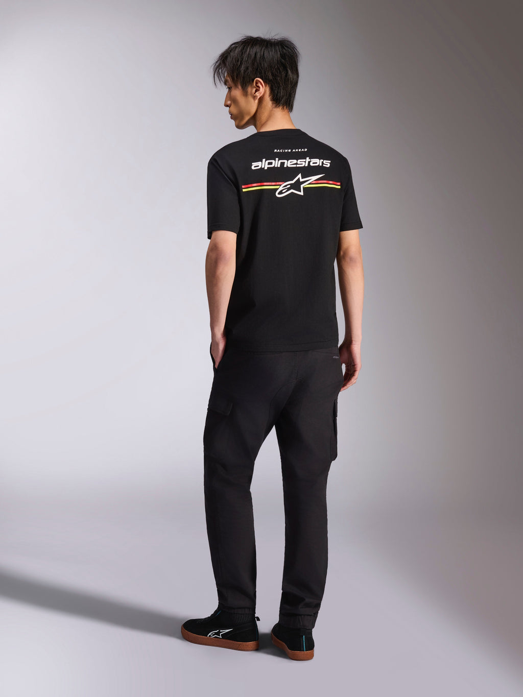 Alpinestars Lanes CSF Tee, t-shirt de manga curta preta, vista das costas com logótipo Alpinestars branco e grafismo de riscas vermelhas, laranja e amarelas, streetwear casual de desportos motorizados usada com calças cargo pretas