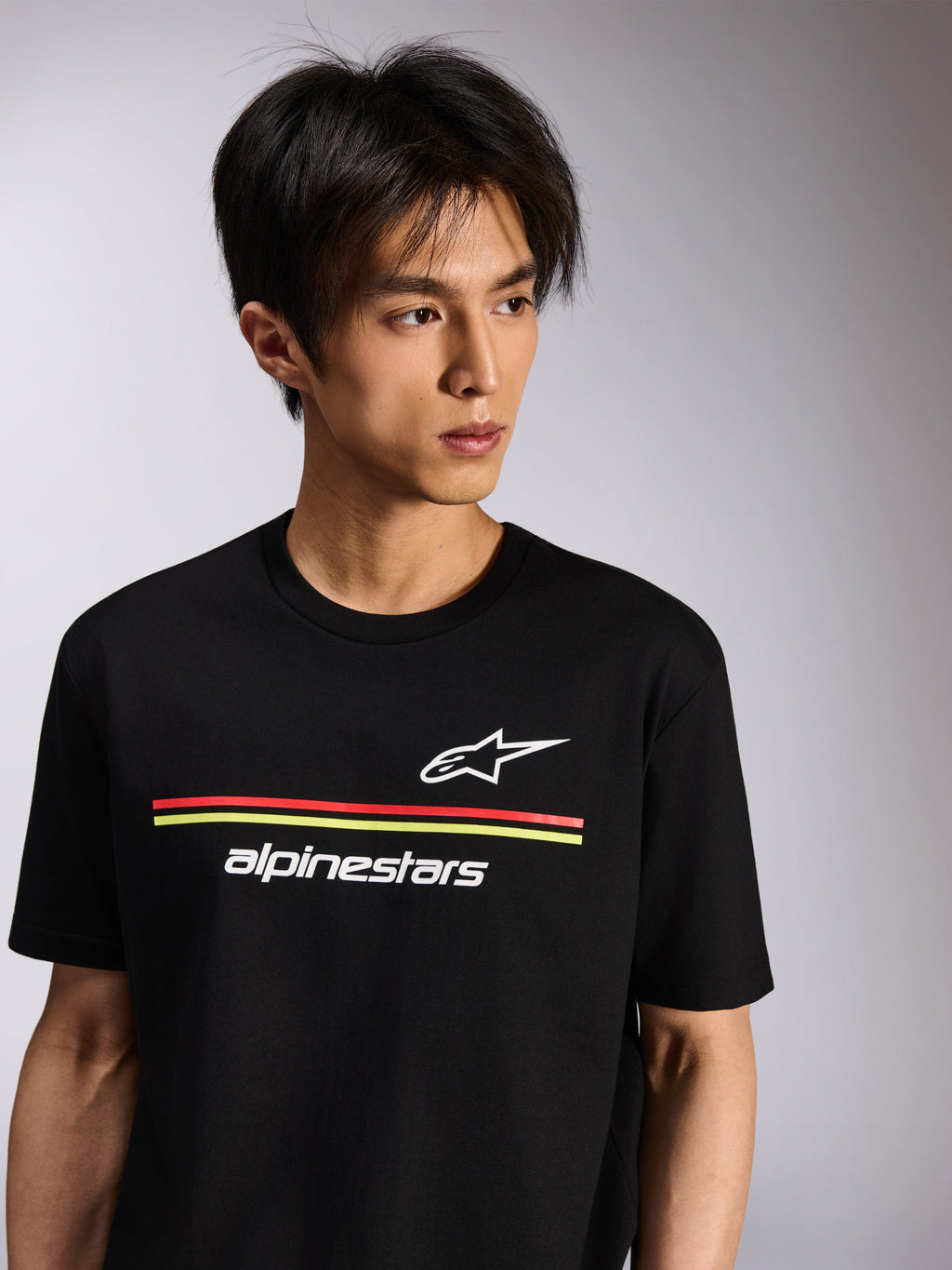 Alpinestars Lanes CSF Tee, t-shirt de manga curta, preta, com logótipos Astars e Alpinestars brancos e riscas vermelhas e amarelas, vestuário casual motorsport usado por um modelo
