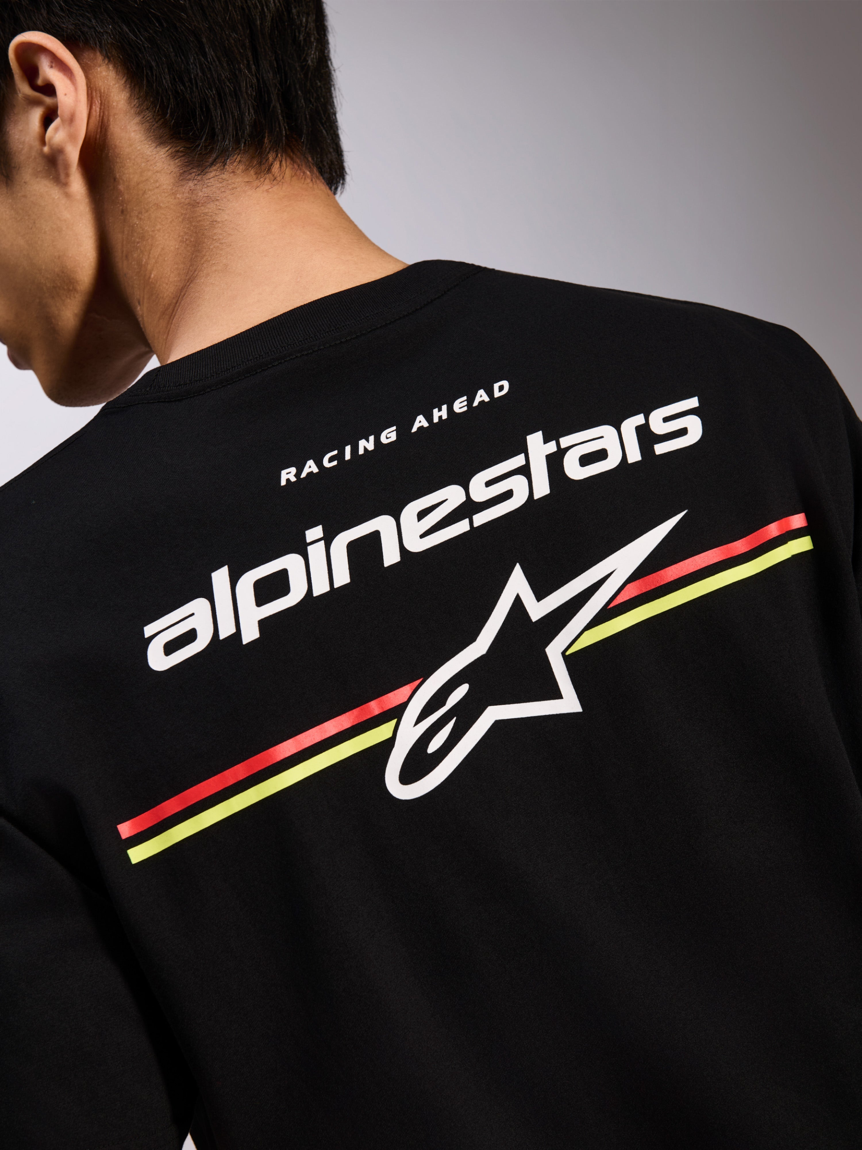 T-shirt Alpinestars Lanes CSF, t-shirt de manga curta preta, gráfico nas costas com logótipos Alpinestars e Astars a branco sobre riscas vermelhas e amarelas, streetwear casual de desportos motorizados