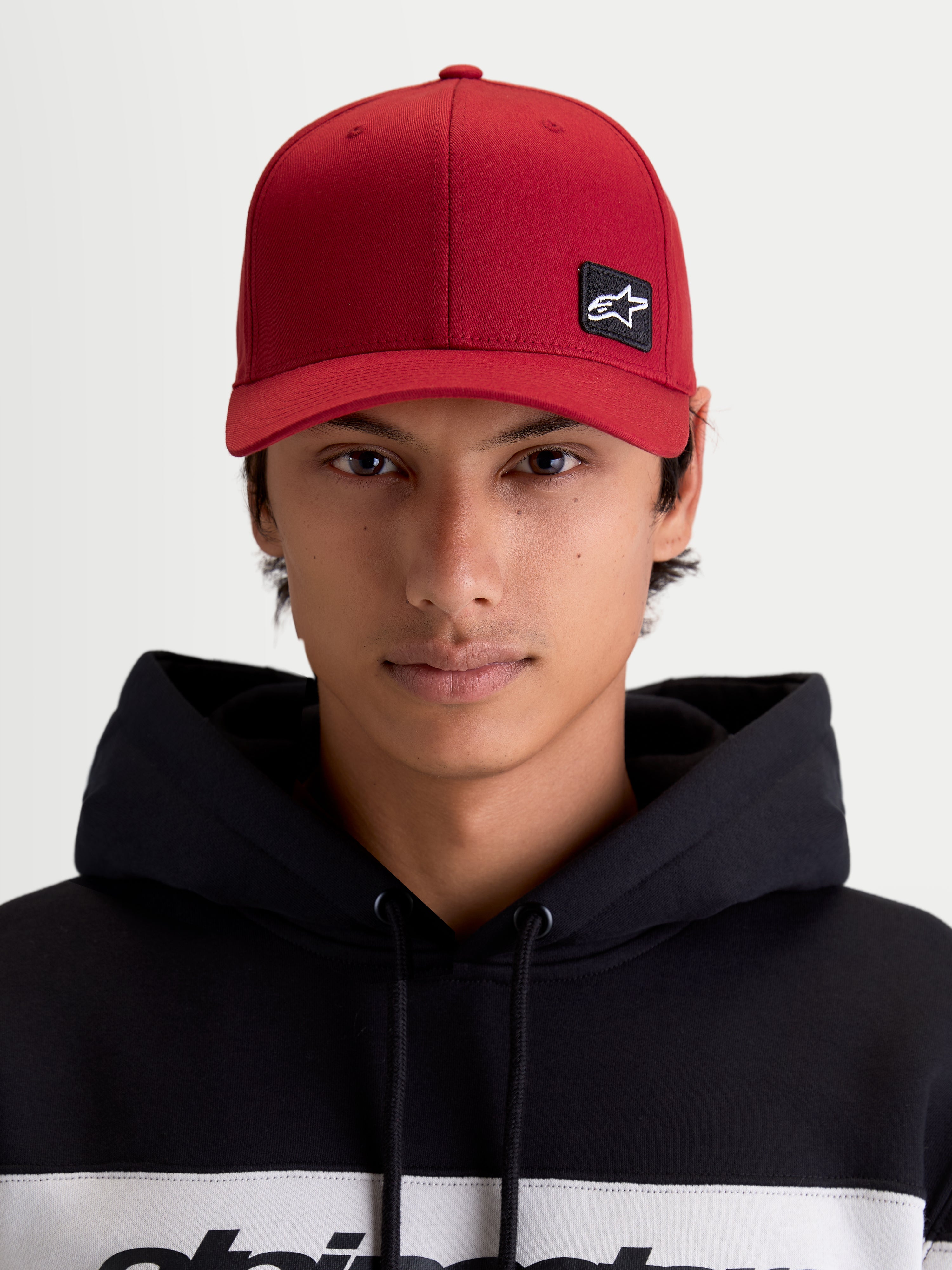 Alpinestars chapéu Pivot, boné de sportswear unissexo, vermelho escuro, vista frontal no modelo com patch do logótipo Astars bordado, aba curva, coroa estruturada e construção em sarja resistente.