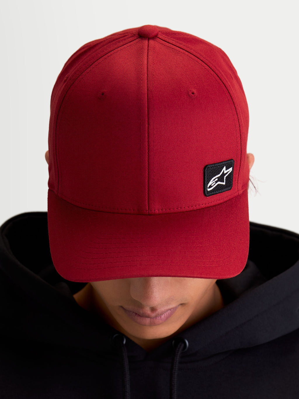 Alpinestars Chapéu Pivot, boné sportswear casual unissexo, vermelho escuro, tecido em sarja resistente com aba curva e coroa estruturada, pequeno patch preto do logótipo Astars bordado, vista no modelo.