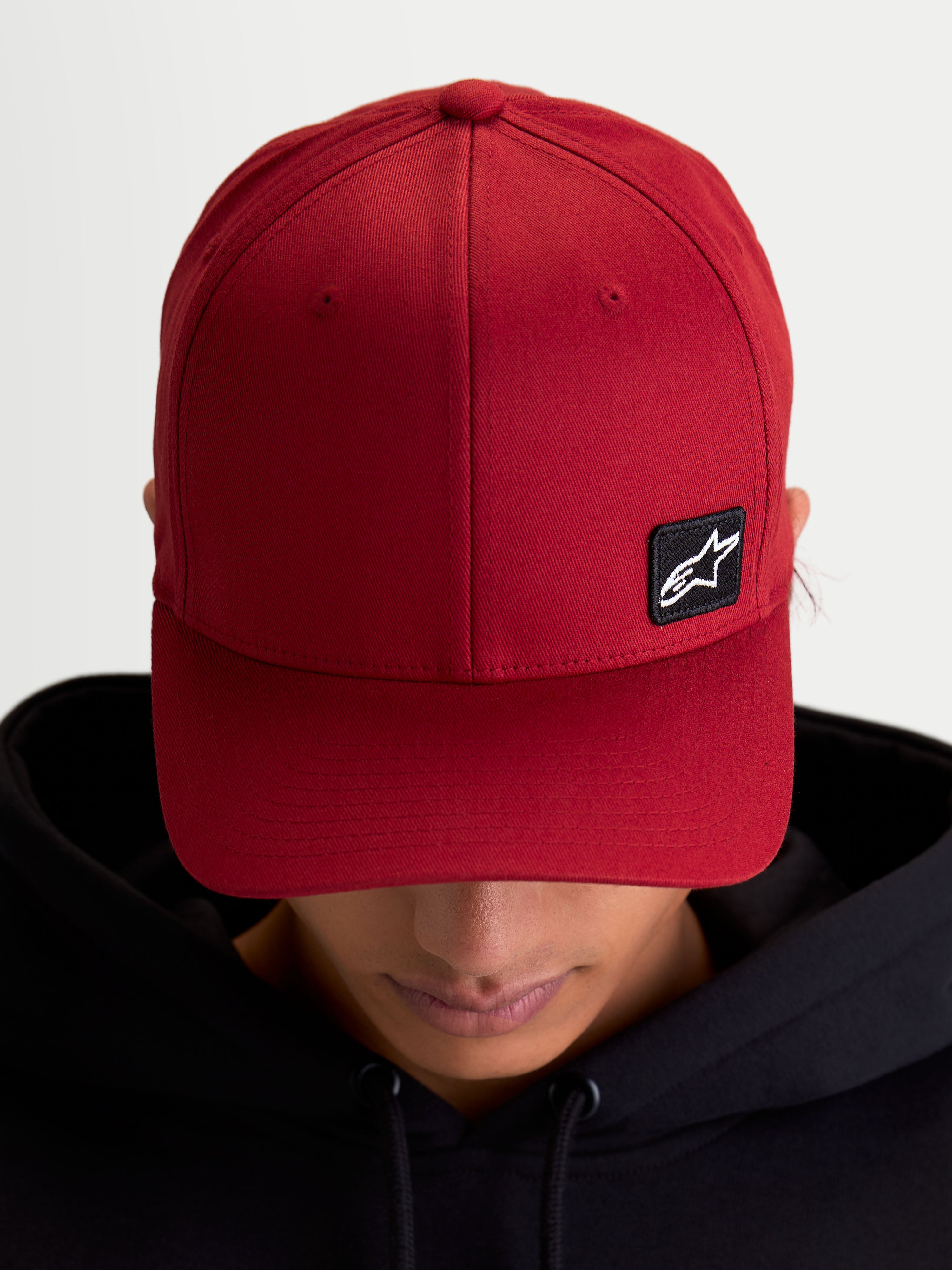 Alpinestars Chapéu Pivot, boné sportswear casual unissexo, vermelho escuro, tecido em sarja resistente com aba curva e coroa estruturada, pequeno patch preto do logótipo Astars bordado, vista no modelo.