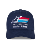 Alpinestars Trifecta Snapback Hat, boné azul-marinho com pala curva, logótipo frontal bordado com estrela branca e riscas tricolores, texto branco 'Racing Ahead' e 'Goal One Vision', copa estruturada, acessório casual inspirado no desporto motorizado