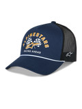Boné Alpinestars Finisher Trucker, azul-marinho e preto, pala curva com detalhe de corda branca, gráfico frontal de bandeiras de xadrez Alpinestars com logótipo dourado e texto "Racing Ahead", bordado lateral do logótipo Astars, acessório casual de desportos motorizados
