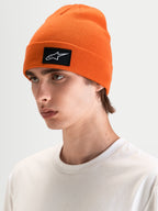 Alpinestars Augment Cuff gorro, gorro de malha laranja com patch tecido do logótipo Astars preto e branco, usado por um modelo em sportswear casual