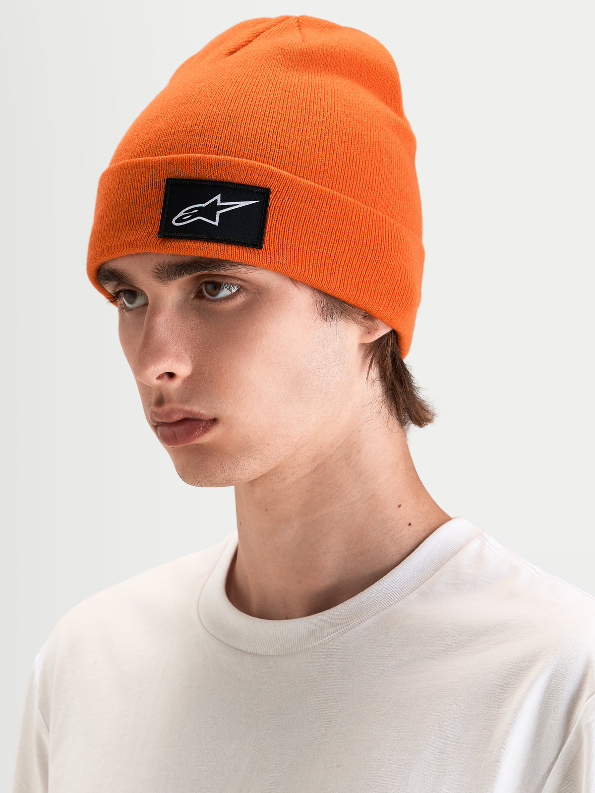 Alpinestars Augment Cuff gorro, gorro de malha laranja com patch tecido do logótipo Astars preto e branco, usado por um modelo em sportswear casual