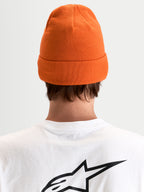 Alpinestars Augment Cuff gorro, gorro de malha laranja com silhueta de ajuste profundo e design com dobra, vista traseira num modelo a usar uma t-shirt branca com logótipo preto Astar
