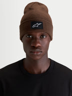 Alpinestars Gorro Augment Cuff, gorro de sportswear, castanho, com patch tecido do logótipo Alpinestars na bainha, vista frontal num modelo com uma T-shirt preta