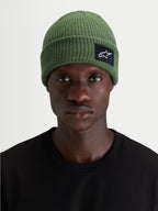 Alpinestars Unload Rib Cuff Beanie, sportswear knit winter hat, green, worn by a model showcasing the shallow-fit silhouette and SAstars woven front patch