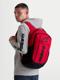 Alpinestars GFX Boss, mochila urban sportswear de 20L, vermelha e preta, mostrada num modelo a usar um casaco com capuz cinzento. Inclui construção em poliéster 600D e logótipo Astars em relevo de silicone. Ideal para o dia a dia.