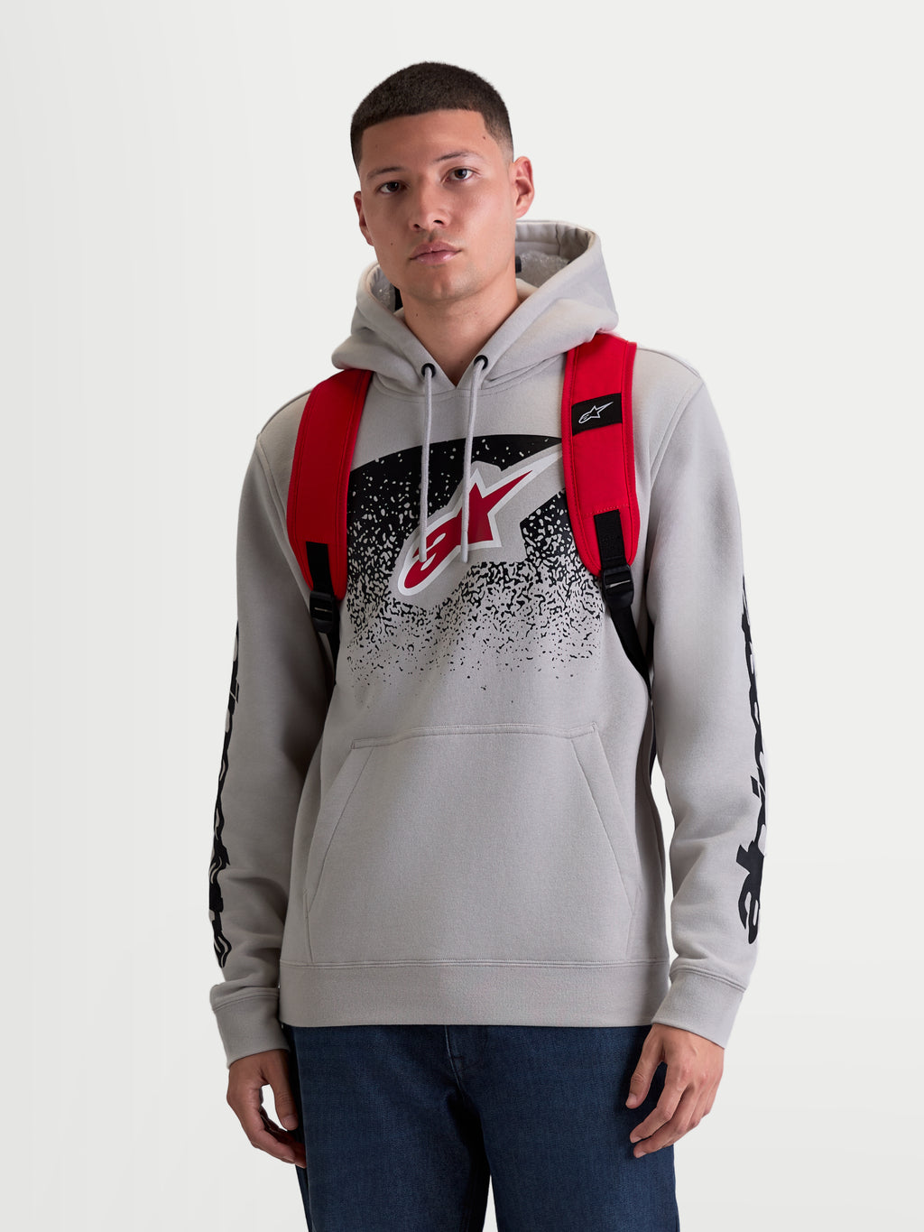 Alpinestars Mochila GFX Boss, mochila sportswear urbana de 20L, para homem e mulher, vermelha e preta, em poliéster 600D resistente. Vista frontal no modelo, apresentando alças de ombro ajustáveis em rede respirável e logótipo Astars em silicone em relevo.