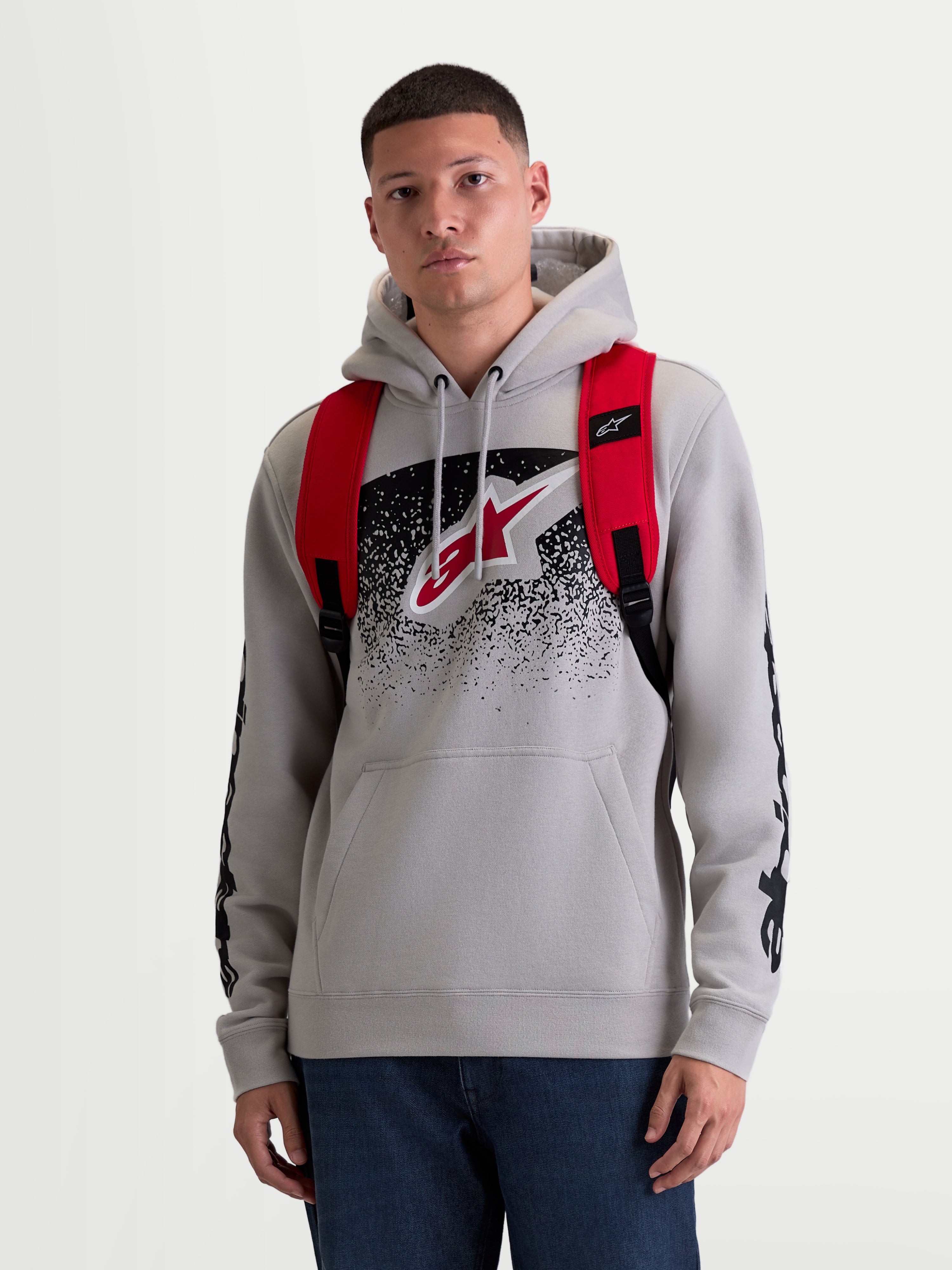 Alpinestars Mochila GFX Boss, mochila sportswear urbana de 20L, para homem e mulher, vermelha e preta, em poliéster 600D resistente. Vista frontal no modelo, apresentando alças de ombro ajustáveis em rede respirável e logótipo Astars em silicone em relevo.