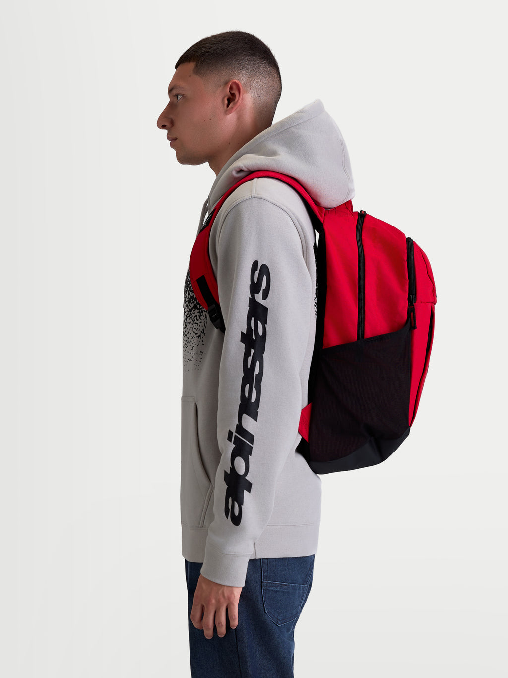 Alpinestars Mochila GFX Boss, mochila de uso diário sportswear, vermelha e preta, capacidade de 20L, construção em poliéster 600D com bolsos laterais em rede e alças almofadadas, mostrada num modelo para uso urbano.