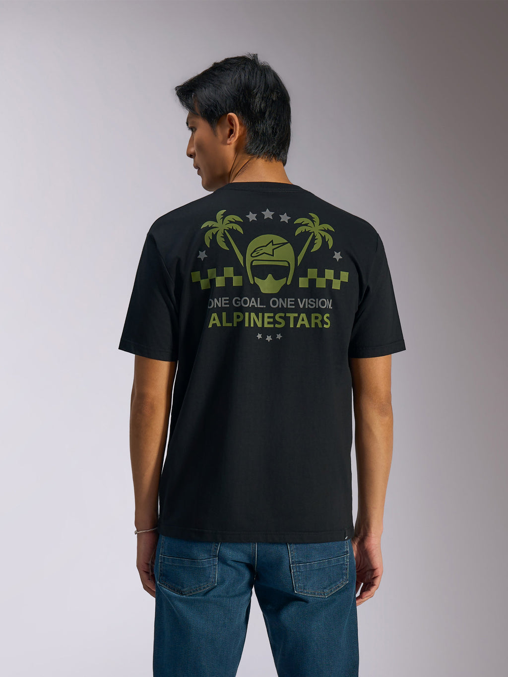 Alpinestars Order CSF Tee, Short Sleeve T-Shirt, Black, Back View, Olive Green Graphic with Palm Trees and Helmet Logo, 'ONE GOAL. ONE VISION. ALPINESTARS' text, paired with blue jeans, casual motorsport streetwear