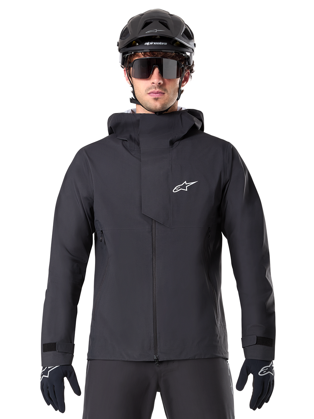 Alpinestars A-Dura Elite Waterproof Jacket, Black, Mountain Bike Jacket, High-collar design with hood, Front zipper with protective chest flap and white logo, Worn with black helmet and cycling gloves, Technical weather protection for trail riding