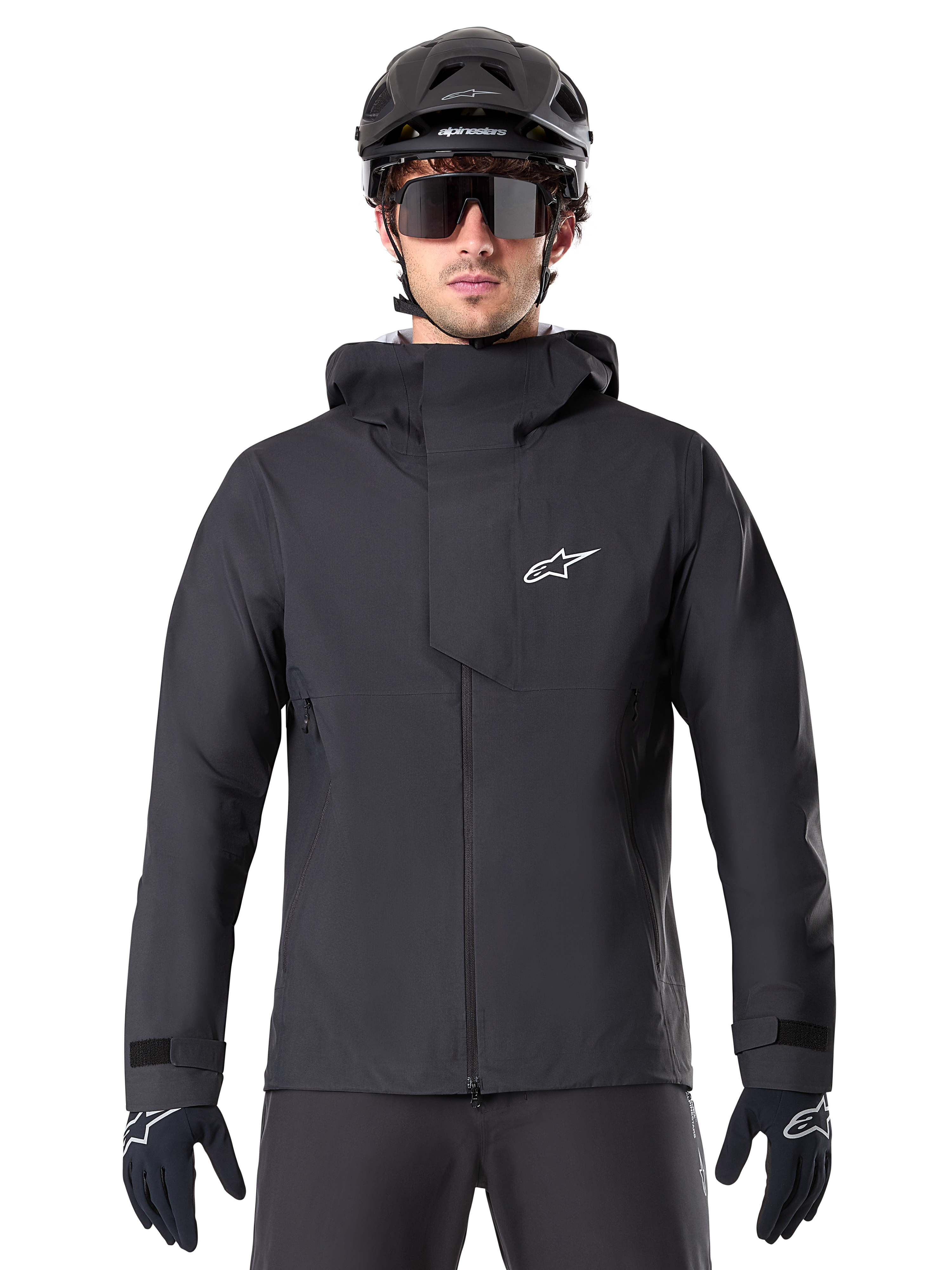 Alpinestars A-Dura Elite Waterproof Jacket, Black, Mountain Bike Jacket, High-collar design with hood, Front zipper with protective chest flap and white logo, Worn with black helmet and cycling gloves, Technical weather protection for trail riding