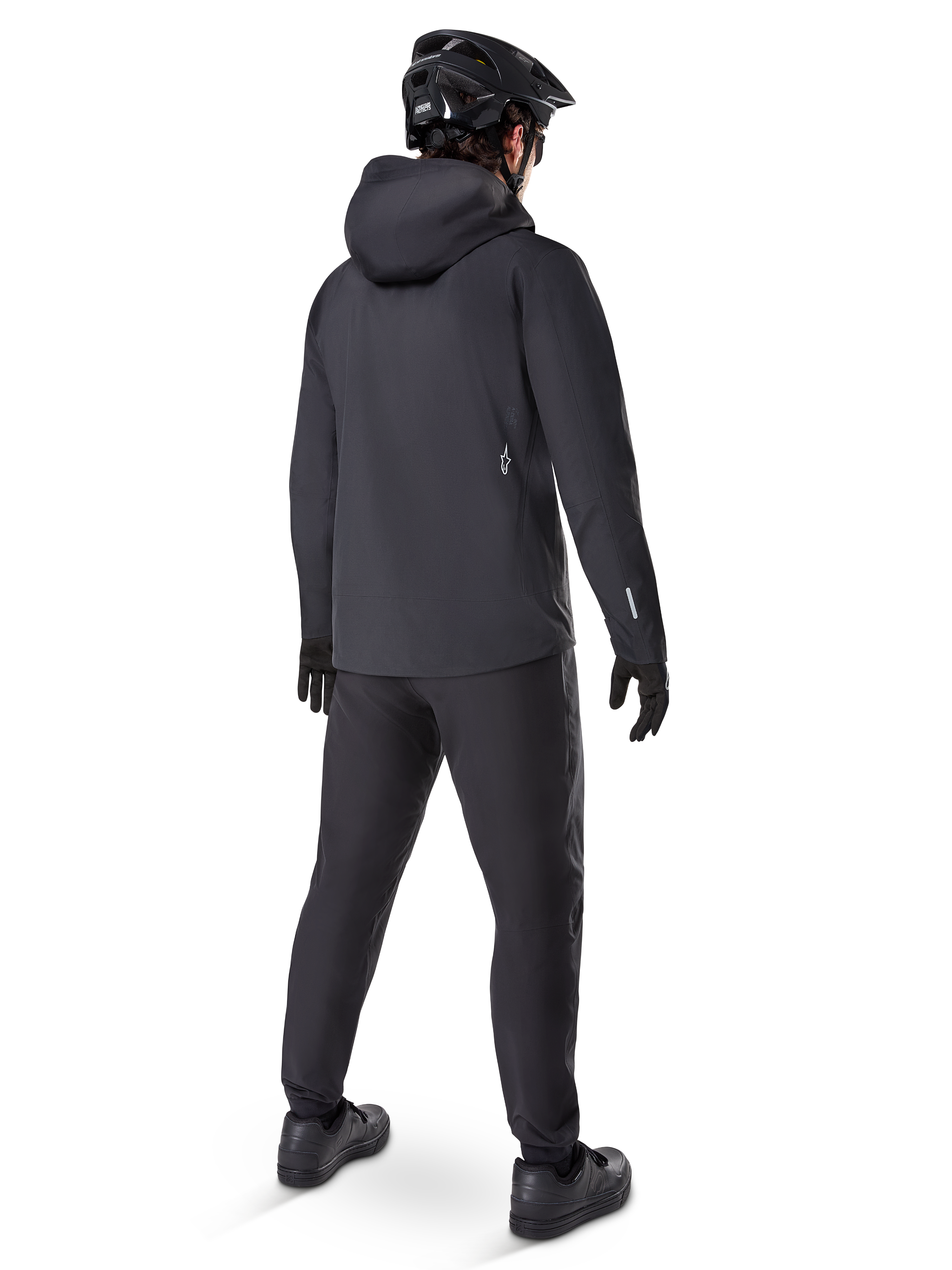 Alpinestars A-Dura Elite Waterproof Jacket, Black, rear view showing over-the-helmet hood and longer drop tail hem, paired with matching black MTB pants, gloves, and helmet for complete all-weather trail protection.