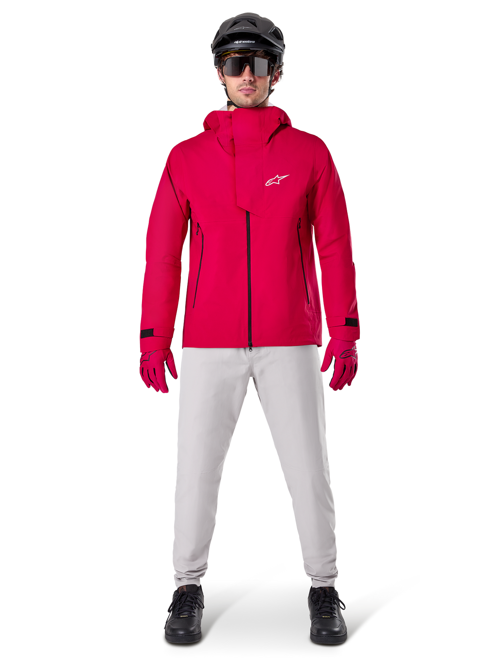 Casaco Impermeável Alpinestars A-Dura Elite, Vermelho Fluo, casaco técnico de BTT usado com um capacete de BTT preto, óculos de sol, luvas vermelhas a condizer e calças cinzentas claras, vista de corpo inteiro de equipamento de ciclismo para todas as condições meteorológicas