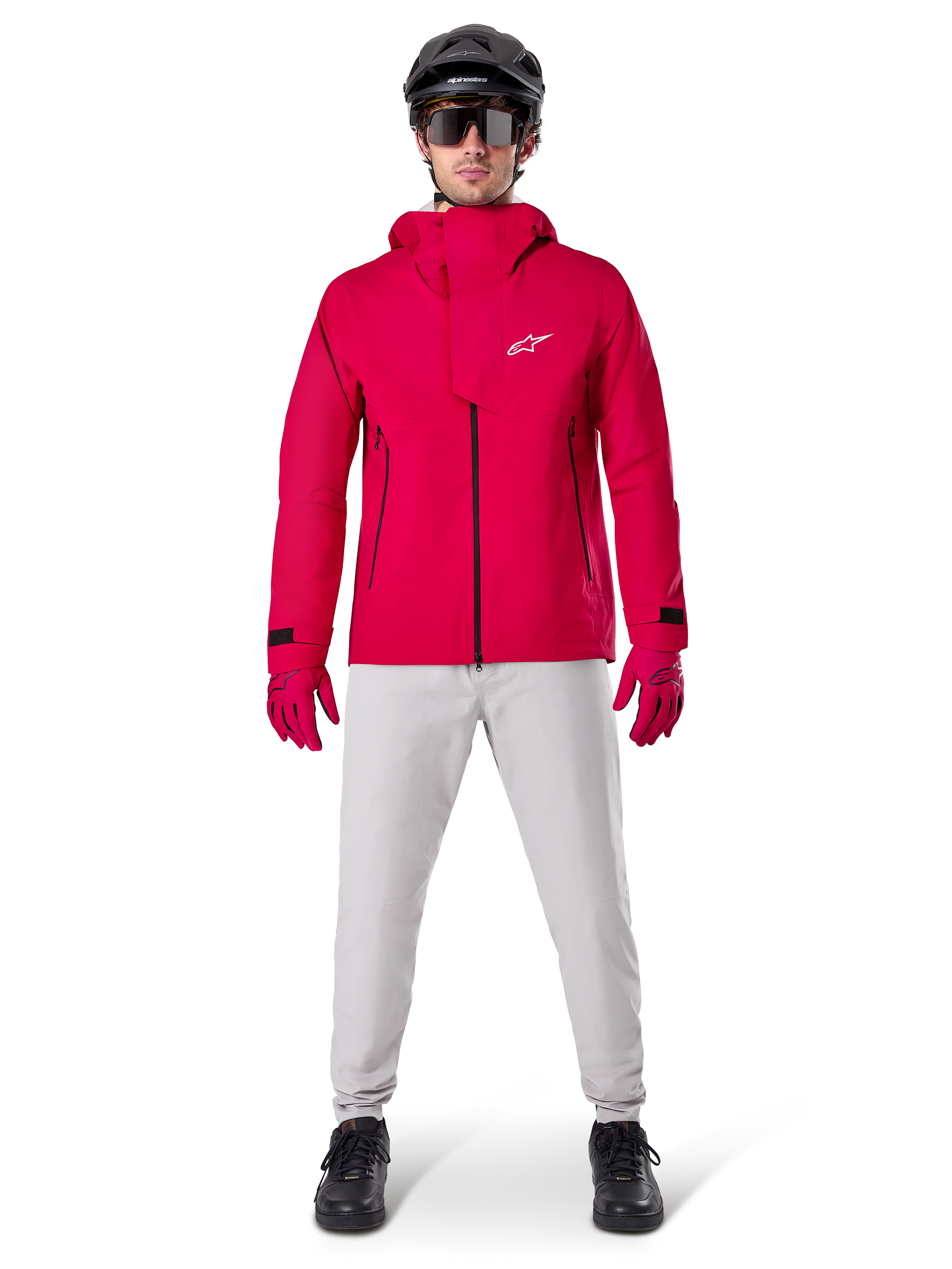 Casaco Impermeável Alpinestars A-Dura Elite, Vermelho Fluo, casaco técnico de BTT usado com um capacete de BTT preto, óculos de sol, luvas vermelhas a condizer e calças cinzentas claras, vista de corpo inteiro de equipamento de ciclismo para todas as condições meteorológicas