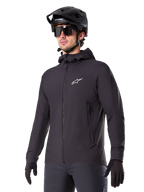 Alpinestars A-Dura Thermal Jacket, Black Cycling Jacket, hooded design with front zipper, white star logo on chest, worn with black mountain bike helmet and gloves, sporty performance gear for cold weather trail riding
