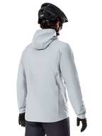 Alpinestars A-Dura Thermal Jacket, Cinzento Titanium, vista traseira de um ciclista a usar o casaco térmico com capuz, combinado com um capacete de BTT preto e luvas pretas, com um pequeno logótipo Alpinestars na parte inferior das costas, concebido para a prática de BTT em climas frios.