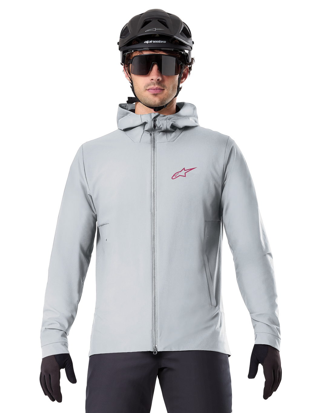 Alpinestars A-Dura Thermal Jacket em Titanium, casaco de ciclismo cinzento claro com capuz e logótipo de estrela vermelho no peito, usado por um ciclista com capacete de BTT preto, óculos de sol e luvas, equipamento térmico para mountain biking