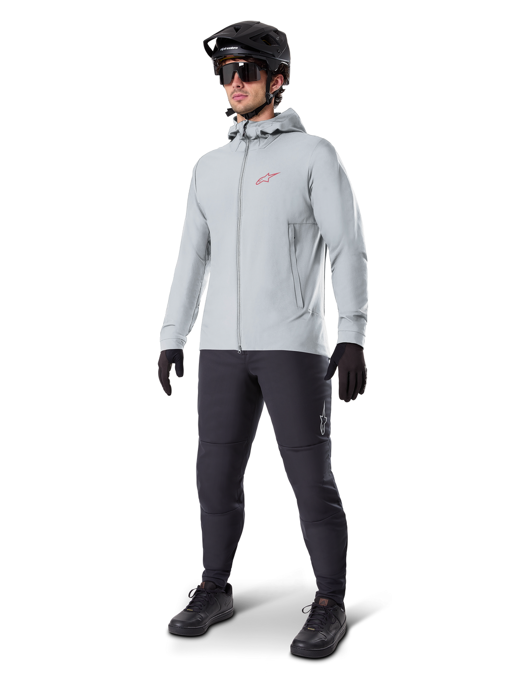 Casaco Térmico Alpinestars A-Dura em Titanium, casaco de ciclismo cinzento claro com capuz e um logótipo Alpinestars vermelho no peito, usado por um homem com capacete de BTT preto, óculos de sol, calças cinzento-escuras e luvas pretas, equipamento profissional de BTT