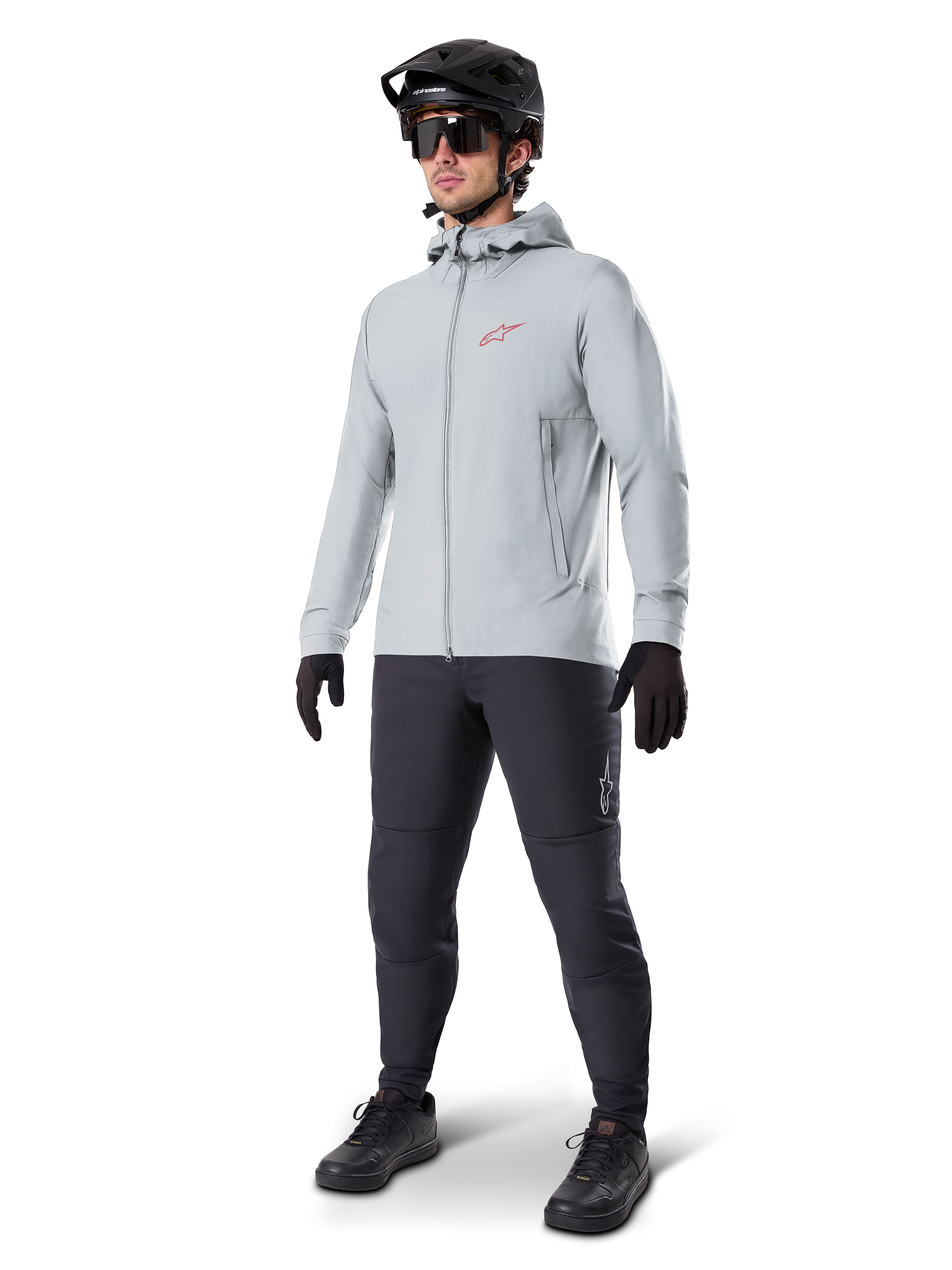 Casaco Térmico Alpinestars A-Dura em Titanium, casaco de ciclismo cinzento claro com capuz e um logótipo Alpinestars vermelho no peito, usado por um homem com capacete de BTT preto, óculos de sol, calças cinzento-escuras e luvas pretas, equipamento profissional de BTT