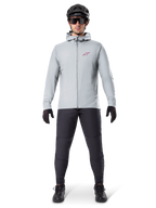 Casaco Térmico Alpinestars A-Dura, cinzento Titanium, casaco de ciclismo usado com calças de BTT pretas, luvas e capacete, com um pequeno logótipo de estrela vermelha no peito e fecho de correr frontal completo, equipamento isolado leve para condução fora de estrada