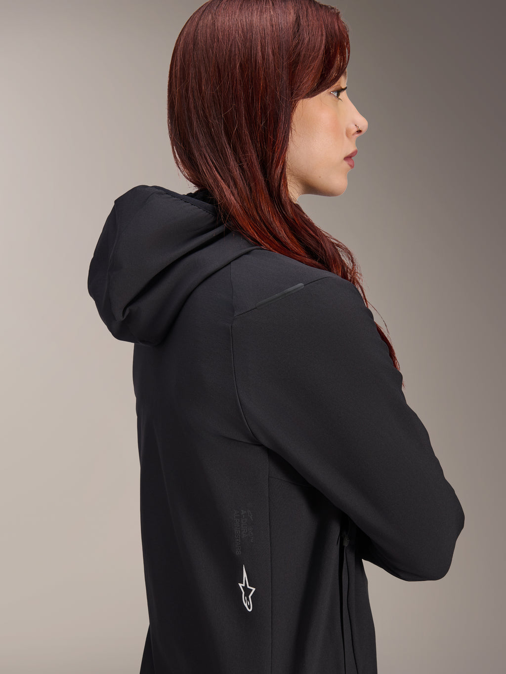 Alpinestars Stella A-Dura Thermal Jacket, Women's Cycling Jacket, Black, side profile of a woman with red hair wearing the jacket, features an integrated hood and white Alpinestars star logo on the side, lightweight insulated thermal gear for MTB.