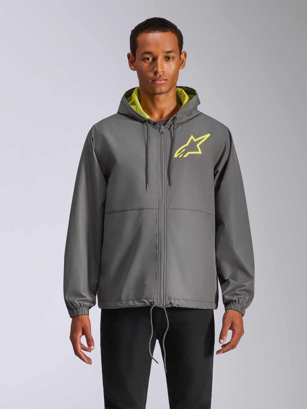 Alpinestars Speeder Chromium Windbreak Jacket, casaco corta-vento cinzento com capuz, logótipo de estrela amarelo néon, interior do capuz verde-limão, punhos elásticos, cordões ajustáveis, fecho de correr frontal, estilo casual de desportos motorizados