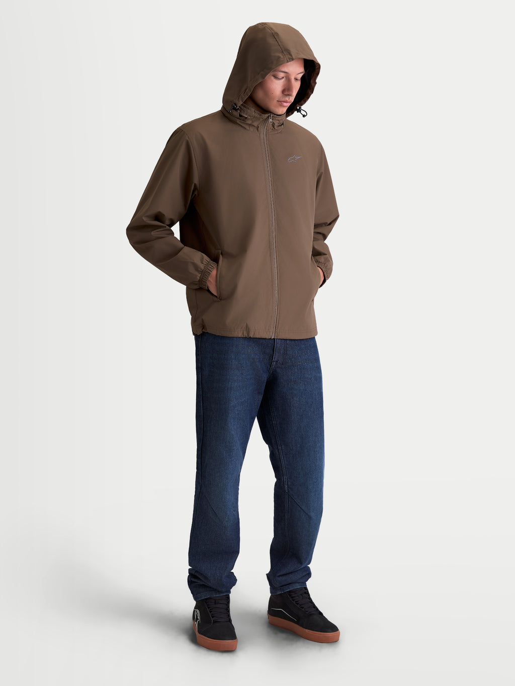 Alpinestars Casaco Overhaul Racer, casaco de sportswear leve para homem, castanho, com capuz e pequeno logótipo Astars no peito, modelo vestido com calças de ganga e sapatos pretos.