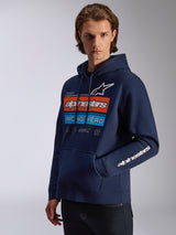 Alpinestars Harken Hoodie, azul marinho, vestido por modelo, com um grafismo arrojado no peito com o design 'Racing Ahead' em laranja e azul, logótipo Alpinestars na manga, bolso canguru e capuz com cordão