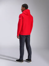 Alpinestars Frontal Hoodie, hoodie vermelho de lã com capuz, vista traseira que mostra o logótipo branco na manga, usado com calças de ganga escuras e sapatos pretos, streetwear casual de desporto motorizado